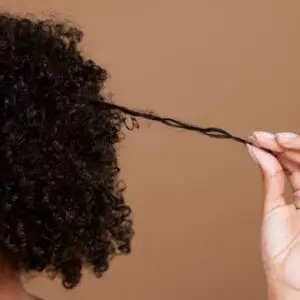 Hair care, beauty and black woman hand with curly hair on brown background in studio. Hair salon, wellness and girl holding curl marketing hair treatment products for growth, natural and healthy hair
